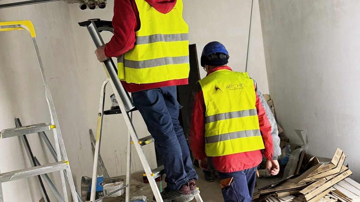 Monterzy w kamizelkach odblaskowych na drabinach przy instalacji wentylacyjnej pod stropem