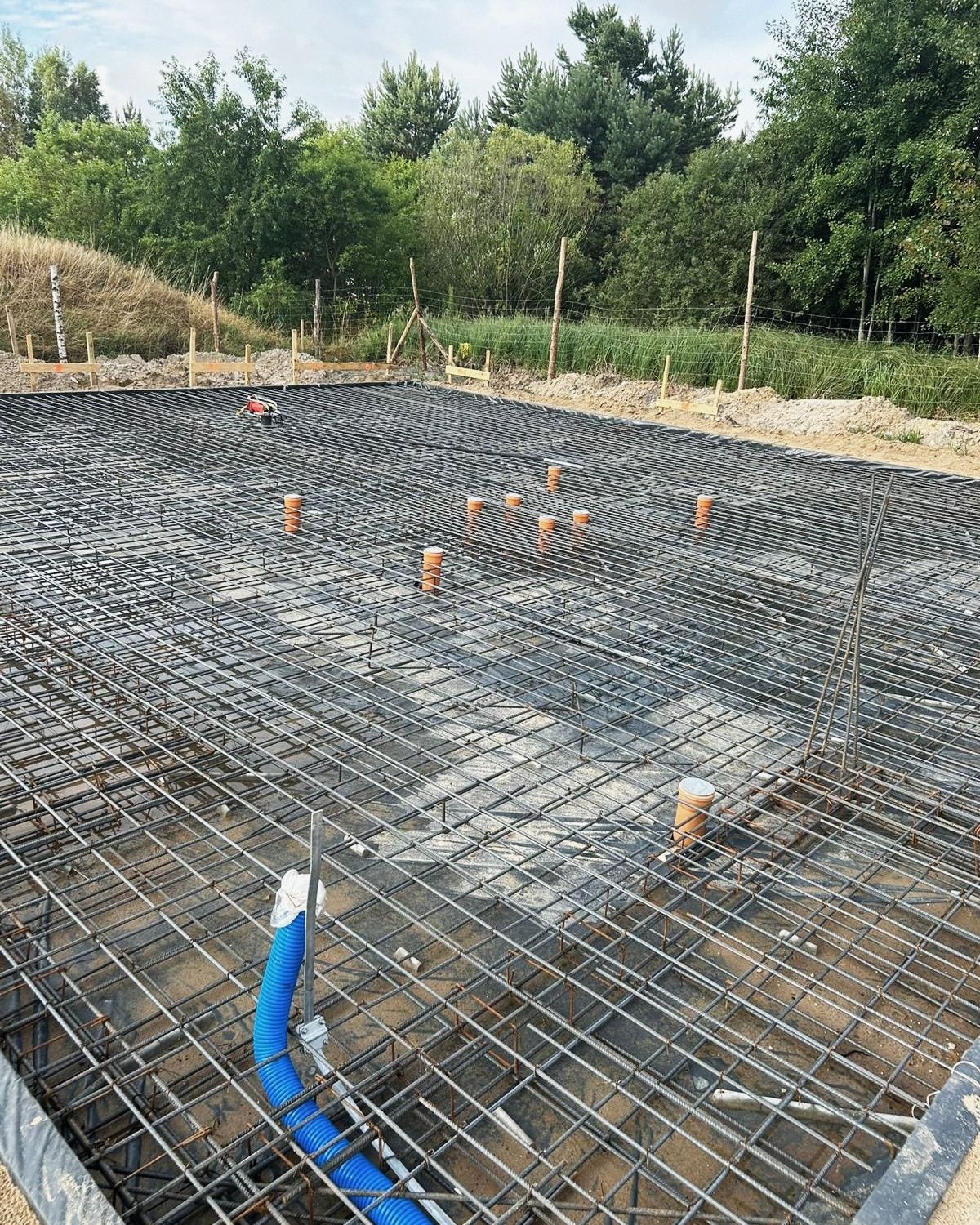 Zbrojenie płyty fundamentowej z pomarańczowymi przepustami rur przed betonowaniem