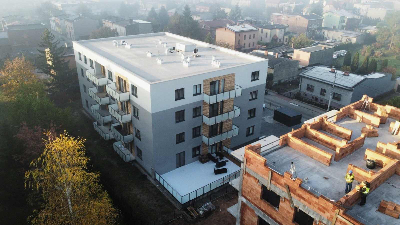 Ukończony budynek wielorodzinny z balkonami, na pierwszym planie mury kolejnego etapu budowy